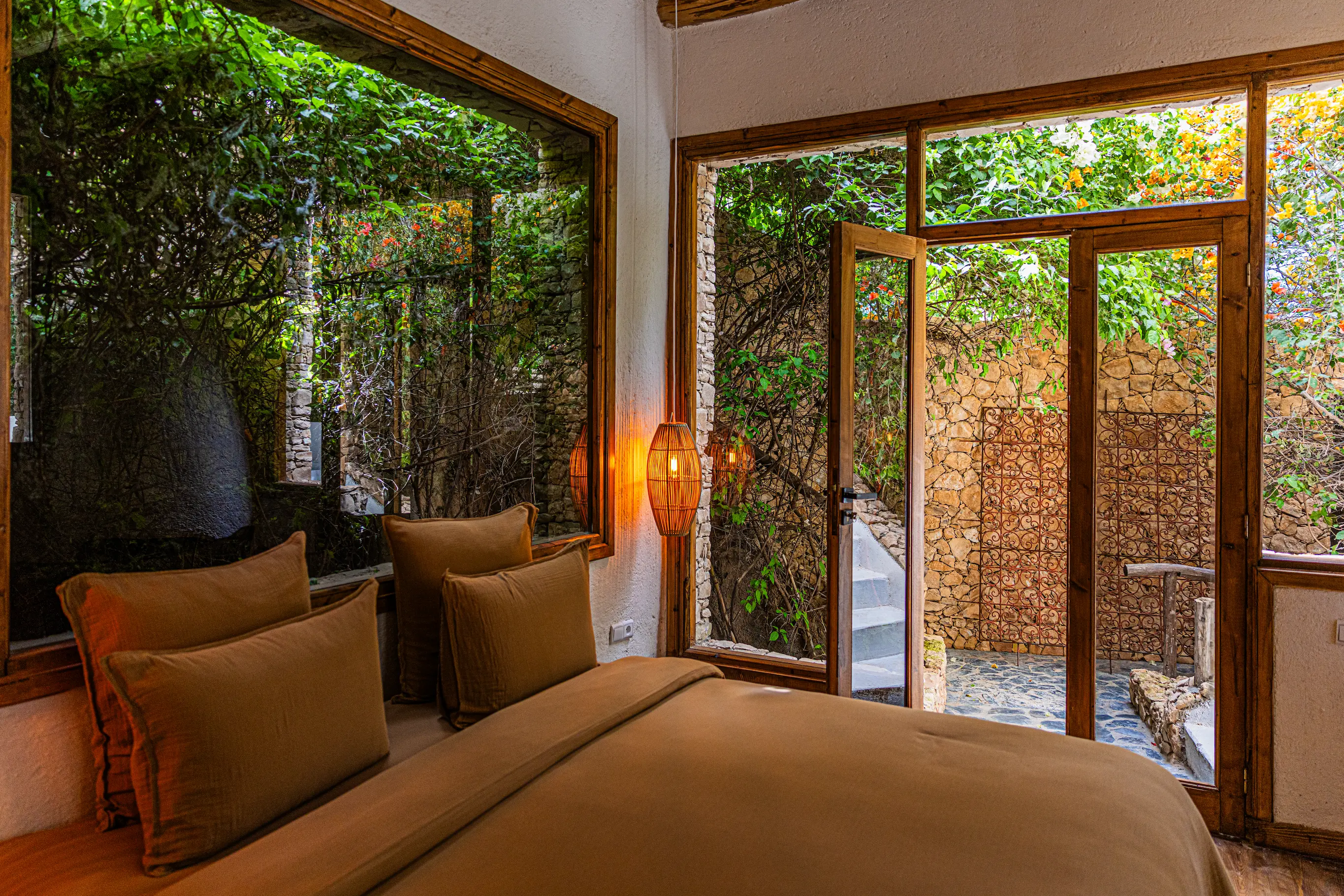 Hôtel Rural de Charme & Suite Vue Jardin | Pure Farmhouse Marrakech Chambre chaleureuse aux tons terreux avec grandes baies vitrées en bois donnant sur une terrasse privée en pierre et le jardin à Pure Farmhouse Marrakech